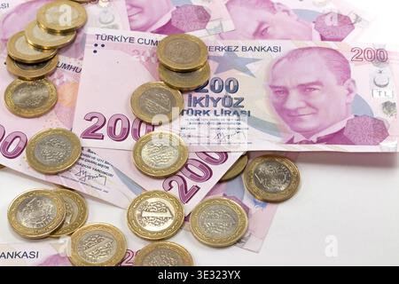 Banconote turche da 200 TL e monete bimetalliche da 1 lira sparse su uno sfondo bianco pulito. Foto Stock
