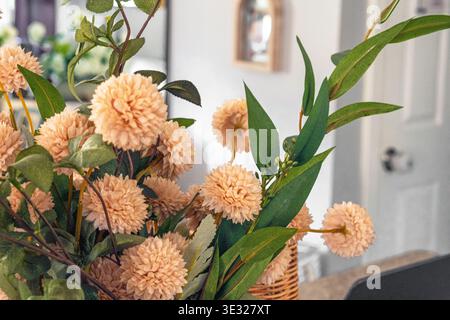 Primo piano di una delicata composizione floreale con morbidi fiori in stile pompon di pesca e fogliame verde in un cesto in tessuto. Contro una casa offuscata i Foto Stock