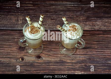 Due bicchieri di frappe di caffè con gocce di cioccolato e wafer roll su un tavolo di legno. Vista dall'alto, disposizione piatta. Foto Stock