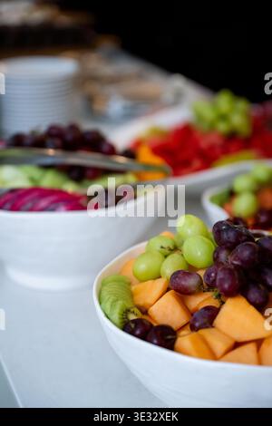 Ciotola per insalata di frutta fresca con uva, melone e kiwi al tavolo a buffet. Insalata di frutta colorata con uva verde e rossa, cantaloupe e kiwi a fette Foto Stock