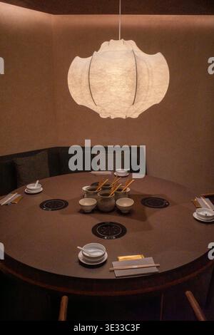 Una calda lanterna è appesa al tavolo da pranzo rotondo. L'area soggiorno presenta un design minimalista e intimo. Il tavolo contiene ciotole, bacchette e piatti piccoli. Centrare in Foto Stock