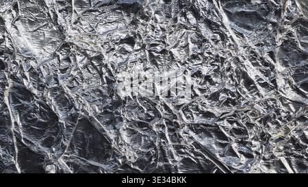 Superficie in lamina di alluminio deformata che mostra una struttura metallica astratta e pieghe riflettenti Foto Stock