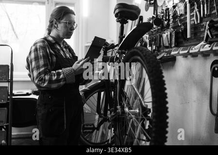 riparatrice che rileva un problema alla sua bicicletta utilizzando un tablet. copia spazio. foto in bianco e nero Foto Stock