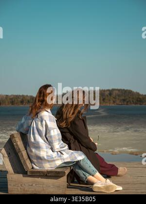 Due giovani donne siedono su una panchina di legno al Kakerdaja Bog Lake Boardwalk Estonia, al sole primaverile Foto Stock