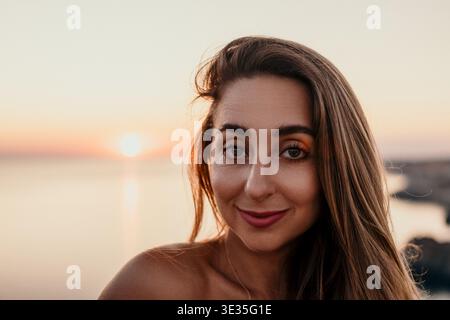Ritratto di donna al tramonto con una giovane donna sorridente durante l'ora d'oro sul mare che rappresenta la pace e la bellezza delle vacanze Foto Stock