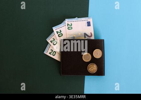 Portafoglio in pelle scura con banconote da 20 euro e monete in euro su sfondo minimalista verde e blu Foto Stock
