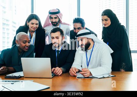 Diversi professionisti internazionali si sono riuniti intorno a un notebook in un moderno ufficio aziendale, collaborando e discutendo di strategie durante un professionista Foto Stock