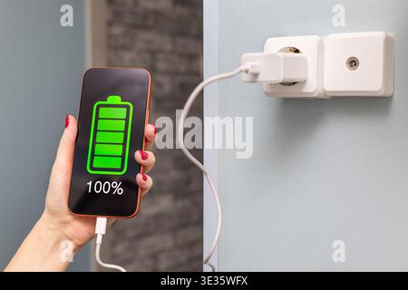 Primo piano delle mani di una donna che ricarica uno smartphone utilizzando un cavo e una porta USB. Una donna carica uno smartphone, primo piano. ricarica un telefono da un ele domestico Foto Stock