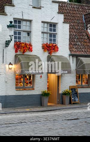 Facciata del negozio di cioccolato con scatole di fiori autunnali su Cobblestone Street, Bruges, Belgio Foto Stock