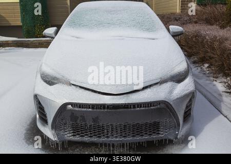 Vista frontale dell'auto passeggeri in argento parcheggiata coperta da una fitta coperta di ghiaccio e neve dopo la pioggia gelida nel tardo inverno, Quebec, Canada Foto Stock