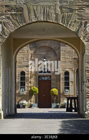 Porta ad arco in pietra con doppie porte marroni e piante in vaso con facciata simmetrica Foto Stock