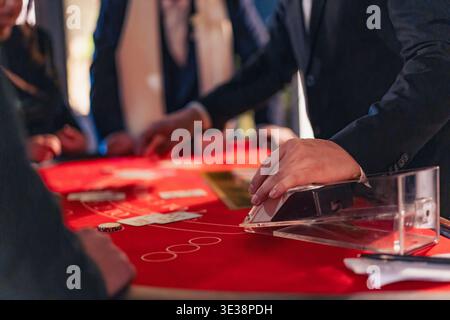 Il mazziere del casinò spara carte sul tavolo del blackjack con i giocatori in giro. Concetto di gioco d'azzardo, rischio e scommesse. Foto Stock