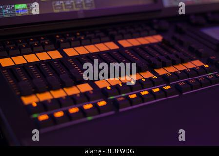 Primo piano di una console di missaggio audio professionale con pulsanti e cursori illuminati in un ambiente di studio buio. Moderne apparecchiature audio Foto Stock