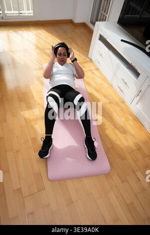 Giovane donna che si allena sul tappetino da yoga con le cuffie e si siede per il benessere Foto Stock