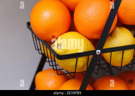 Arance e limoni freschi in un cestino di filo nero. Agrumi sani in un ambiente semplice da cucina. Vitamine naturali e cibo fresco Foto Stock