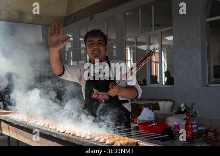 Lo chef griglierà carne spiedata all'aperto, saluterà i visitatori in mezzo al crescente fumo e un ambiente gastronomico vivace in un'informale area pranzo all'aperto. Foto Stock