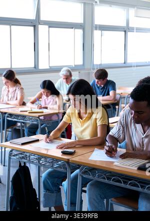 Studenti che sostengono l'esame mentre l'insegnante supervisiona in classe Foto Stock