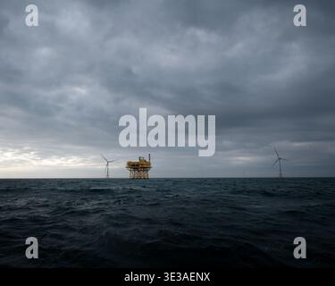 Sottostazione eolica offshore circondata da turbine eoliche sotto nuvole di tempesta scure in mare. Foto Stock