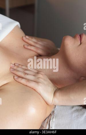 Donna sdraiata su un tavolo da massaggio che riceve un massaggio professionale alla schiena e alle spalle in un rilassante ambiente spa con candele Foto Stock