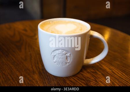 Tazza Starbucks bianca con cuore di latte art su un tavolo da caffè in legno. Londra, Regno Unito, 8 luglio 2023 Foto Stock
