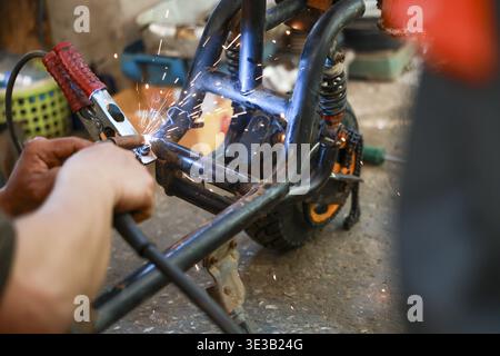 Saldatrice concentrata al lavoro utilizzando uno strumento elettrico di saldatura ad arco per la riparazione di telai metallici. Scintille brillanti volano da metallo caldo durante il processo di fabbricazione in WO Foto Stock