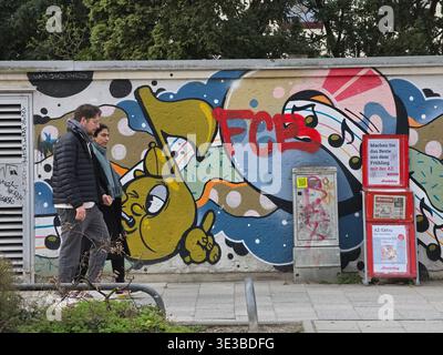 Persone che camminano lungo un muro di graffiti a Monaco, vibrante scena urbana con pedoni che passano attraverso pittoreschi murali di Street art, scritte audaci ed expres Foto Stock