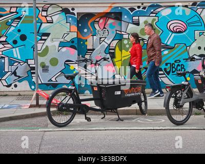 Persone che camminano lungo un muro di graffiti a Monaco, vibrante scena urbana con pedoni che passano attraverso pittoreschi murali di Street art, scritte audaci ed expres Foto Stock