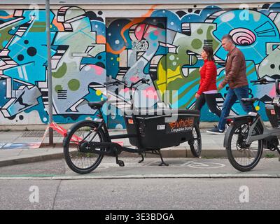 Persone che camminano lungo un muro di graffiti a Monaco, vibrante scena urbana con pedoni che passano attraverso pittoreschi murali di Street art, scritte audaci ed expres Foto Stock