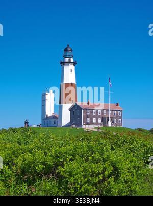 Faro di Montauk Point a Long Island con bandiera americana sul Sunny Blue Sky sopra i terreni costieri Foto Stock