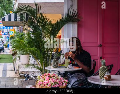 Young Man mangia in un Bright Pink Outdoor Cafe Foto Stock