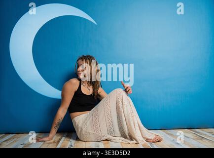 Donna con dreadlock seduto sul pavimento di fronte a una parete blu con luce a mezzaluna Foto Stock