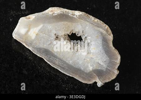 Primo piano di uno strato grezzo di geode riempito di quarzo su sfondo di granito nero Foto Stock