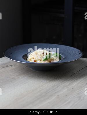 Spaghetti alla carbonara con guanciale croccante e pecorino, serviti su un piatto blu in un raffinato stile da pranzo con illuminazione soffusa. Foto Stock