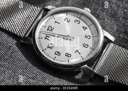 Foto macro di un moderno orologio a una mano con cassa in acciaio inossidabile su un lucente bracciale mesh metallico su sfondo grigio. Design classico in accessori moderni Foto Stock
