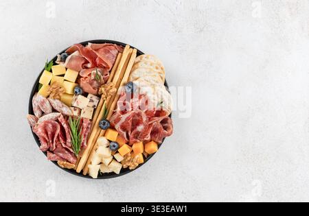 Tagliere di salumi con formaggi assortiti, affettati, cracker, noci su sfondo bianco. Vista dall'alto. Copia spazio Foto Stock