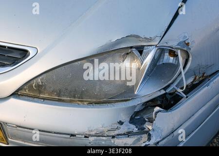 Faro della vettura danneggiato e paraurti anteriore rotto dopo un primo piano di incidente stradale con plastica incrinata e carrozzeria bianca graffiata Foto Stock