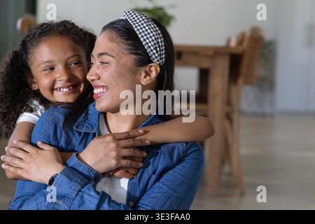 Mamma e bambina afroamericana che sorride indossando un cerchietto a scacchi in denim vicino al tavolo Foto Stock