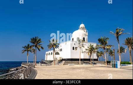La moschea dell'isola bianca si erge in modo prominente lungo la costa del Mar Rosso sulla Corniche di Jeddah in Arabia Saudita, incorniciata da palme tropicali sotto un cielo azzurro. Foto Stock