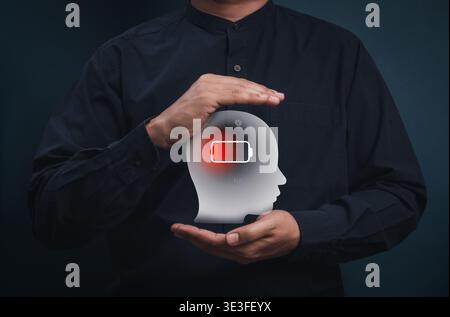 Concetto di sindrome da burnout e esaurimento mentale causati dallo stress cronico sul posto di lavoro. Mani umane che tengono la testa sagoma con l'icona della batteria scarica. Fatig Foto Stock