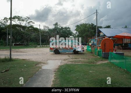 Furgone parcheggiato vicino a una recinzione verde e serbatoio arancione. Cielo nuvoloso sopra gli alberi e campo aperto. L'erba e la sporcizia portano al furgone. Non sono ammessi animali o piante Foto Stock