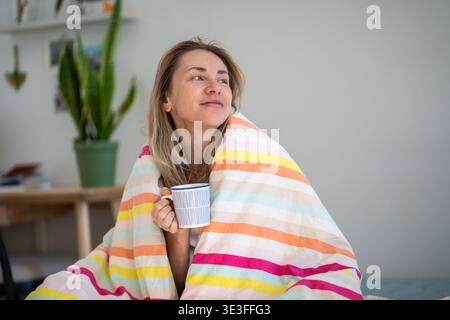 Donna felice e ottimista che beve caffè nel letto confortevole al mattino con un'espressione positiva. Foto Stock