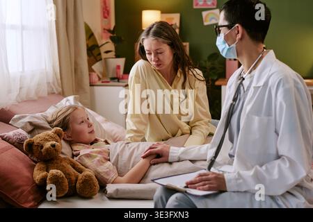 Donna Dottore conforto malato bambino con madre in ospedale stanza Foto Stock
