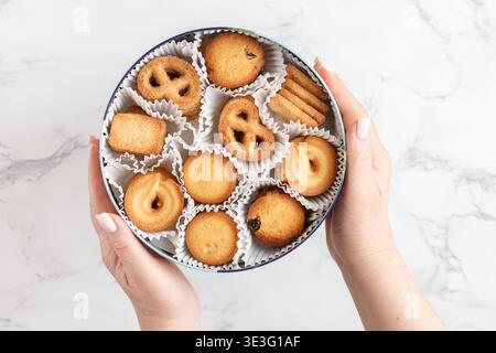 Una donna tiene in mano una scatola di tradizionali biscotti danesi al burro. Biscotti dorati. Messa a fuoco selettiva, vista superiore e Copia spazio Foto Stock