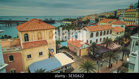 Vicoli stretti che incorniciano edifici coloniali con archi in pietra, facciate intemperie, balconi multilivello e porto turchese oltre, mescolando il patrimonio culturale Foto Stock