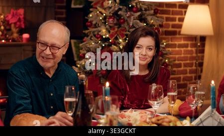 Bella moglie a casa gustando la cena di Natale con i propri cari mentre sorrideva di cuore alla macchina fotografica. Festa felice gente che celebra la vacanza invernale con il cibo tradizionale casalingo. Foto Stock