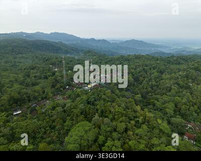 Purworejo Regency, Indonesia - 31 gennaio 2026: Veduta aerea delle lussureggianti foreste verdi che circondano il piccolo villaggio, con due importanti torri cellulari piercin Foto Stock
