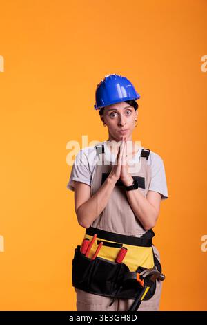 Una donna che fa la preghiera firma con le mani sulla macchina fotografica, implorando e chiedendo nuovi progetti di ristrutturazione. Lavoratrice edile che spera di lavorare sul cantiere e sul progetto di ristrutturazione. Foto Stock