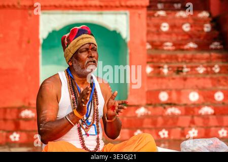 Un ritratto di un uomo in abito tradizionale che canta durante una cerimonia in un ghat a Varanasi, con il fiume Gange in lontananza. Foto Stock