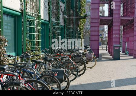 Le biciclette sono parcheggiate lungo un marciapiede vicino a un edificio con facciata verde ed elementi urbani Foto Stock