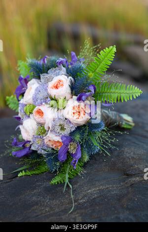 Bouquet nuziale con rose e vegetazione su una superficie rocciosa naturale. Foto Stock